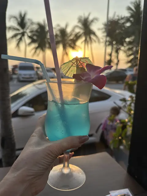 A blue cocktail held toward the sunset